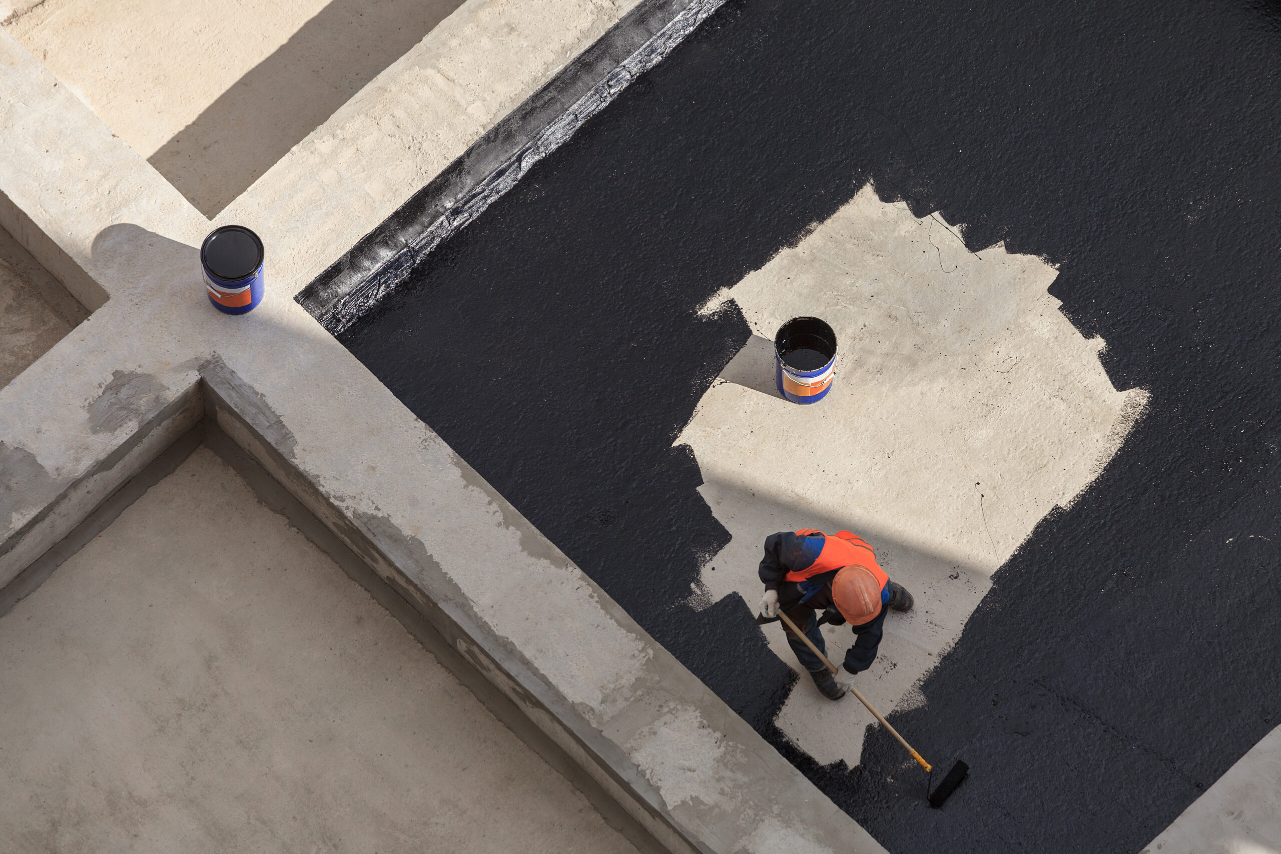 The worker in overalls applies an insulation coating on the concrete surface. View from above. The worker in overalls applies an insulation coating on the concrete surface. View from above.